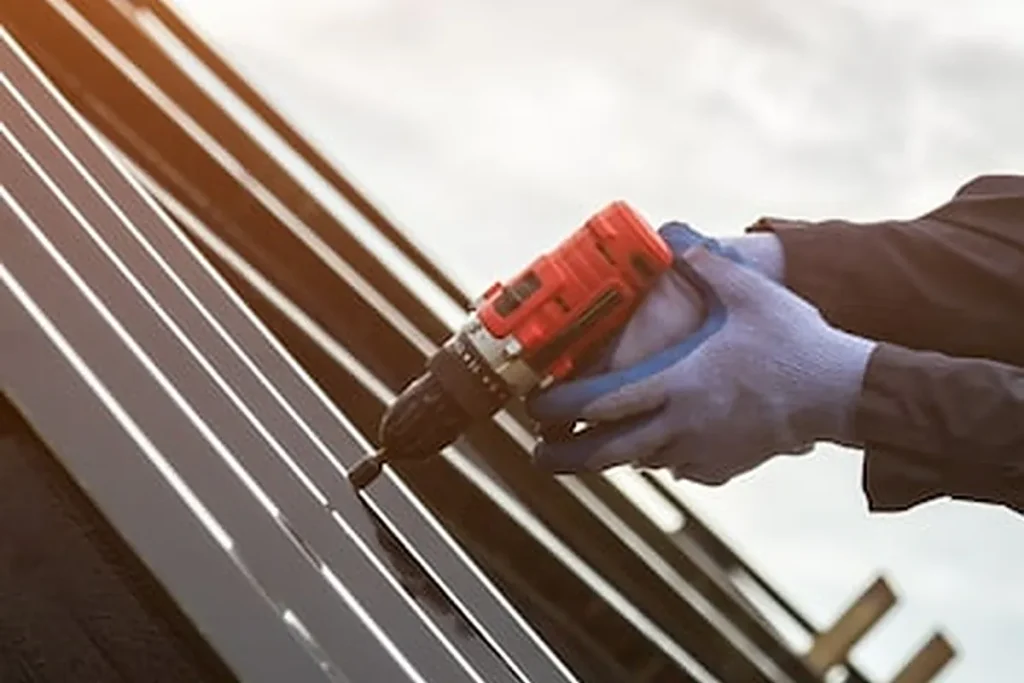 Gloved hands fastening metal roof panels with a cordless drill