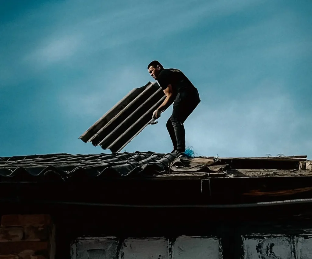Roofer carrying a bundle of shingles across a roof at sunrise